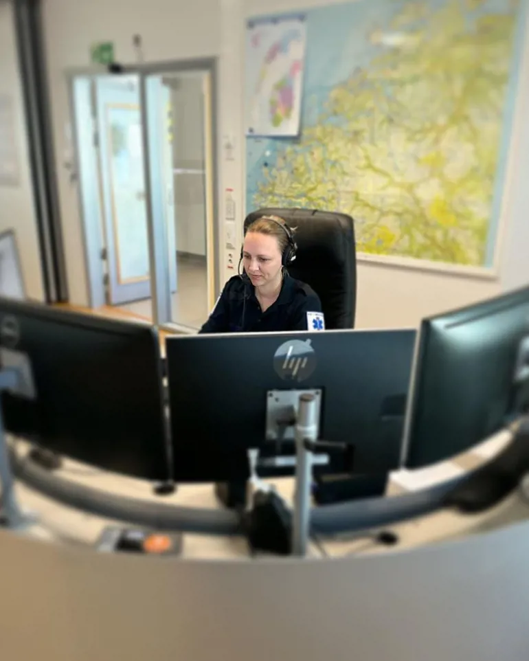 En person som sitter ved et skrivebord med en datamaskin og hodetelefoner på