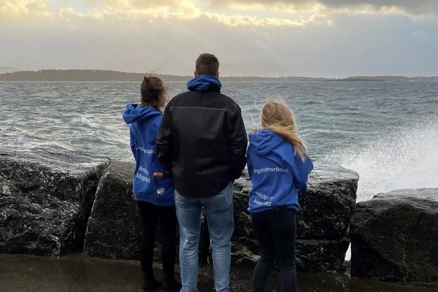 Tre ungdommar står og ser ut over eit ruskete hav